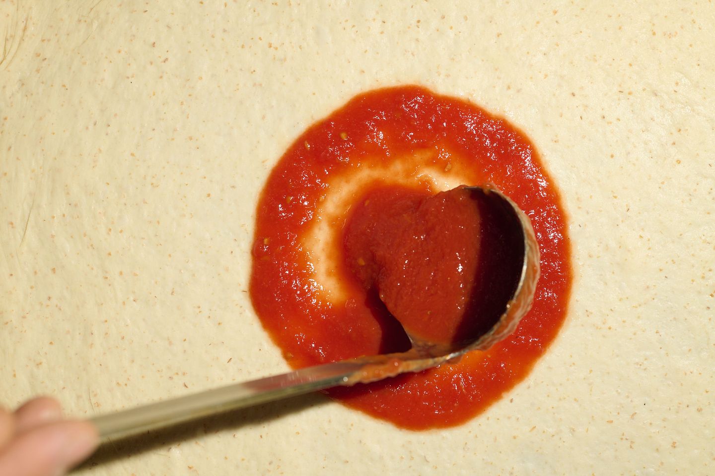 Un mestolo stende il pomodoro San Marzano a spirale sull’impasto
