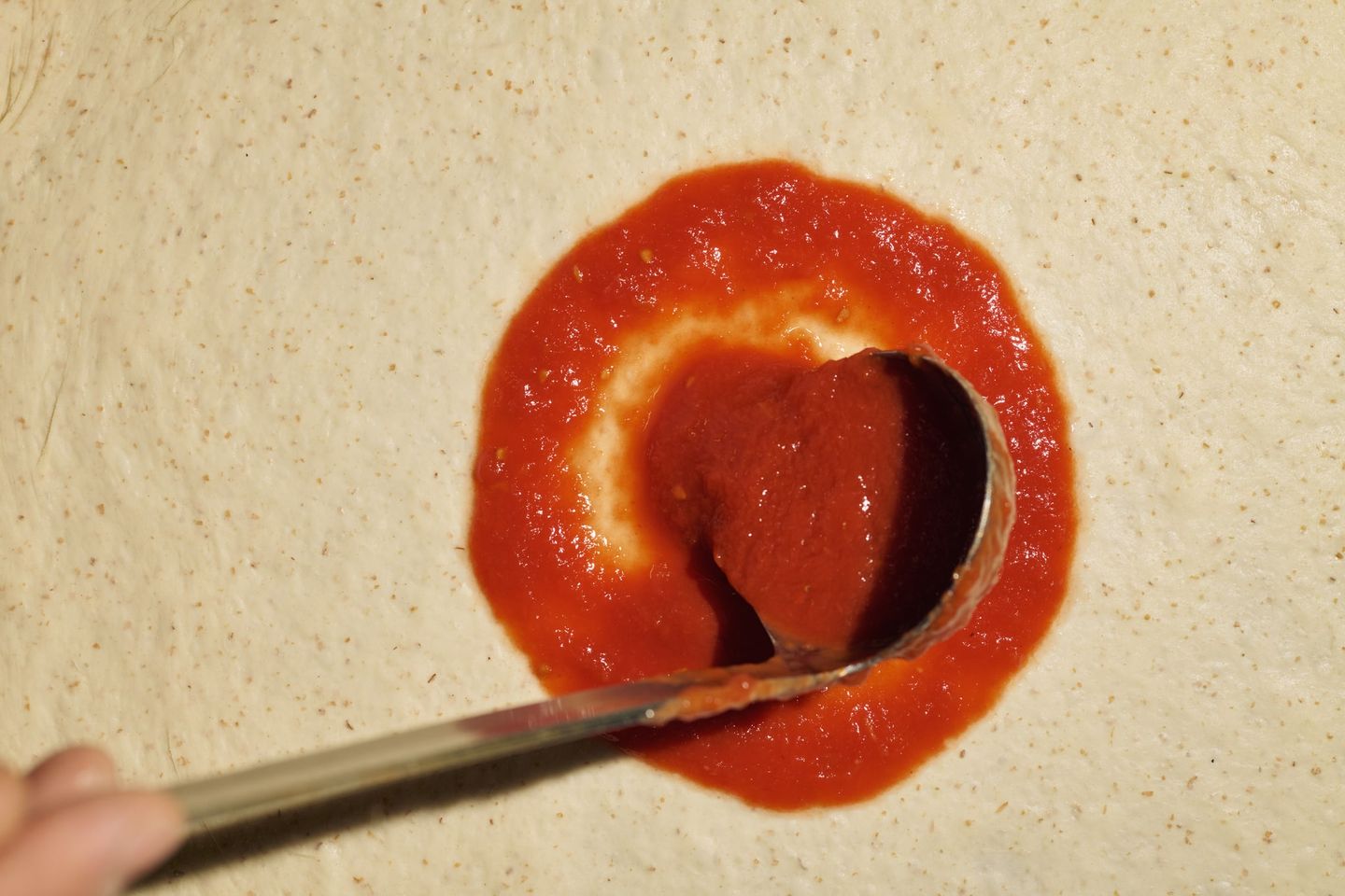 Un mestolo stende il pomodoro San Marzano a spirale sull’impasto