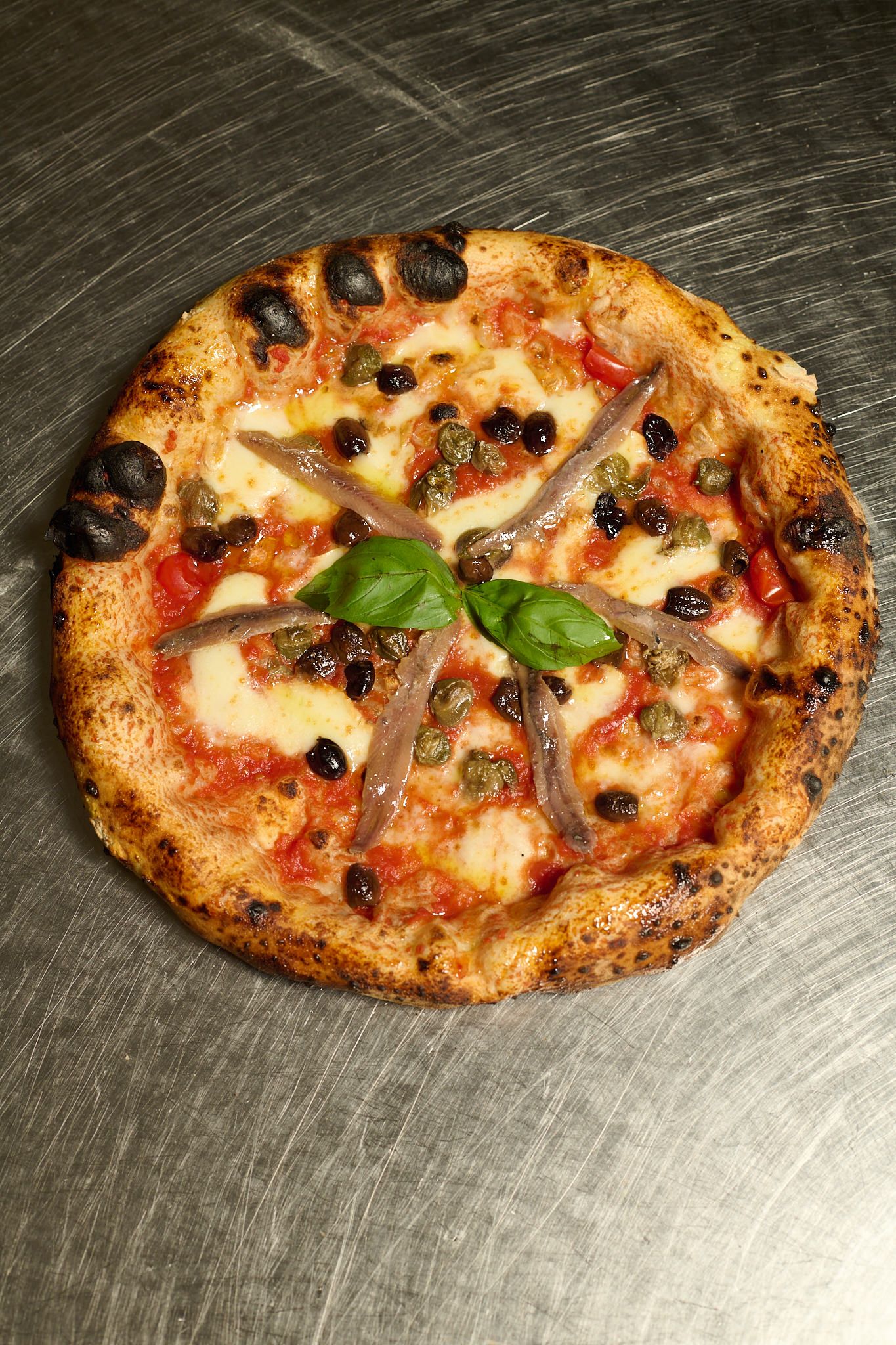 Pizza con acciughe, capperi, olive e basilico, vista dall’alto
