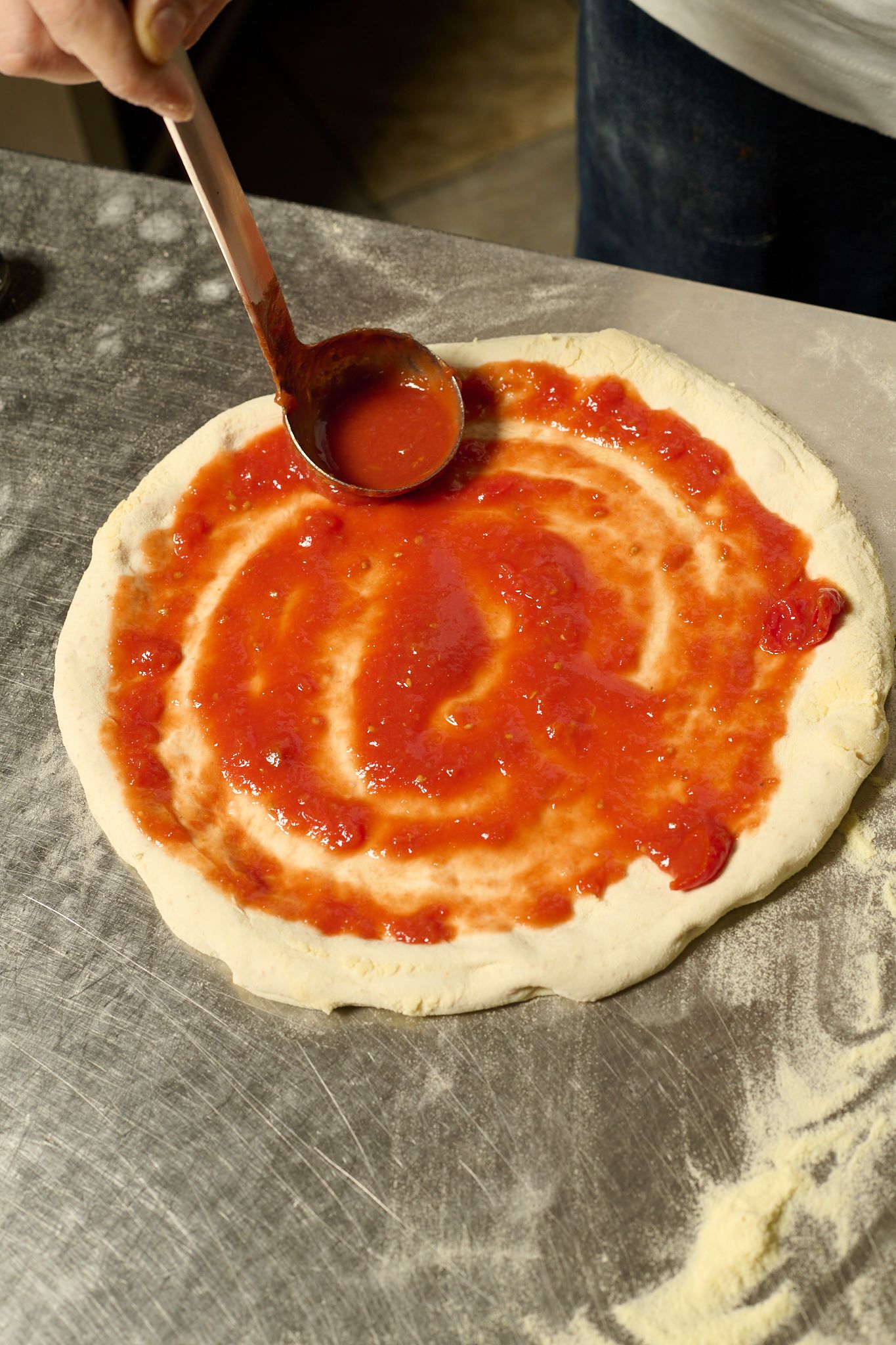 Il pomodoro steso a spirale sull’impasto con un mestolo